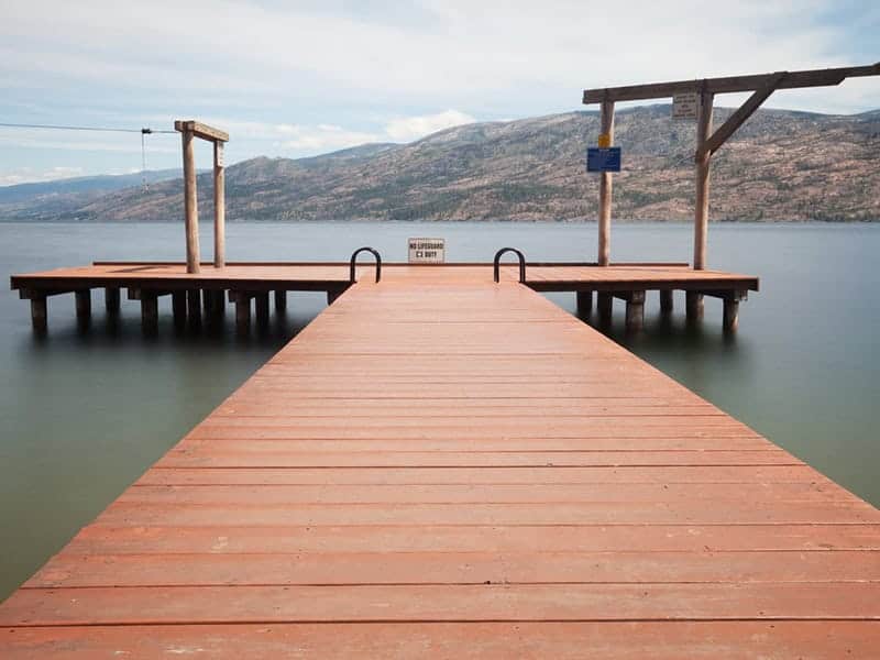 A peaceful wooden dock extending into Okanagan Lake at Peachland, BC's, swim bay with stunning mountain views in the background.